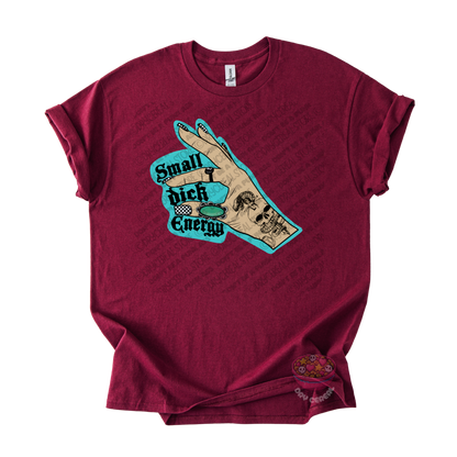 A maroon short-sleeve t-shirt with a graphic of a hand, overlaid with the text 'Small dick Energy' in a teal and black retro font.