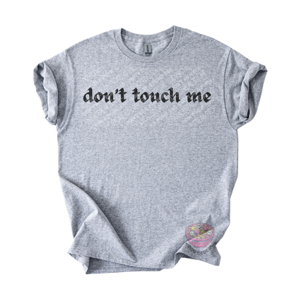 Light gray unisex tee featuring the phrase "don't touch me" in bold gothic black lettering across the chest.