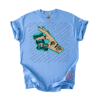 A light blue short-sleeve t-shirt with a graphic on the front showing a hand holding a skull and the text 'Small Dick Energy' in black over a teal background. 