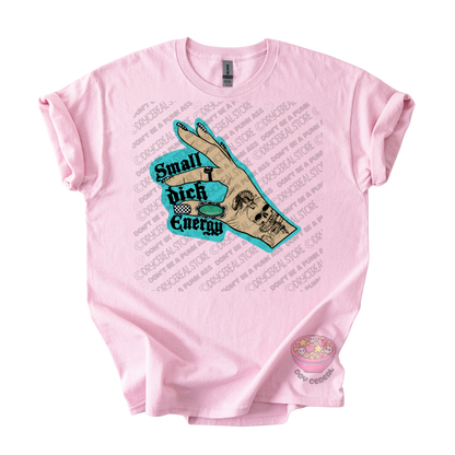 A light pink short-sleeve t-shirt with a graphic print on the front. The graphic features a tan hand holding a turquoise sign that reads 'Small Dick Energy' with a skull design.