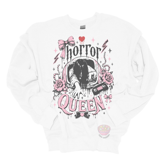 White crewneck sweatshirt featuring a horror-inspired long-haired ghost emerging from a television, surrounded by pink bows, roses, pearls, lightning bolts, and the phrase "Horror Queen."