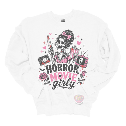 White crewneck sweatshirt featuring a skeleton with a pink bow holding a bloody knife and popcorn, surrounded by horror-inspired movie details, roses, hearts, a VHS tape, retro television, and the phrase "Horror Movie Girly."