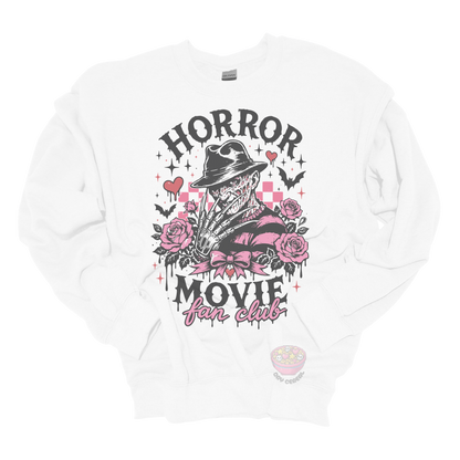 White crewneck sweatshirt featuring a horror-inspired burned slasher character surrounded by pink roses, bats, bows, hearts, and the phrase "Horror Movie Fan Club" in a spooky vintage design.
