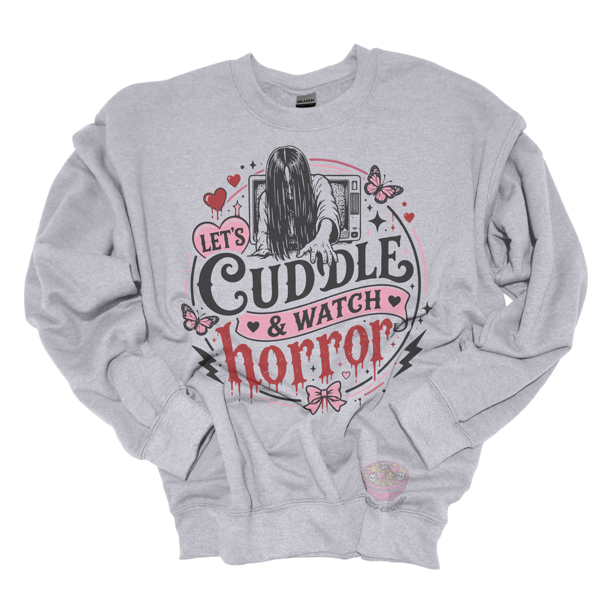 Light grey crewneck sweatshirt featuring a spooky cute horror-inspired design with the phrase "Let's Cuddle & Watch Horror," pink hearts, butterflies, bows, and a creepy long-haired figure emerging from a television.
