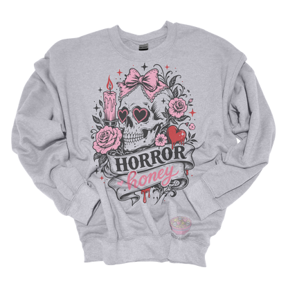 Light gray crewneck sweatshirt featuring a vintage skull with heart-shaped sunglasses, pink bow, roses, candle, dripping heart, and the phrase "Horror Honey" in a spooky gothic design.