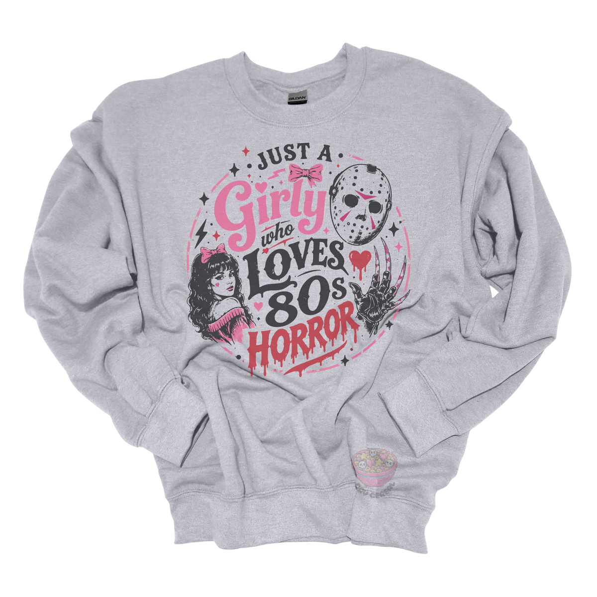 Heather gray crewneck sweatshirt featuring the phrase "Just a Girly Who Loves 80s Horror" with retro horror-inspired artwork including a hockey mask, clawed glove, vintage girl illustration, pink bows, and spooky accents.