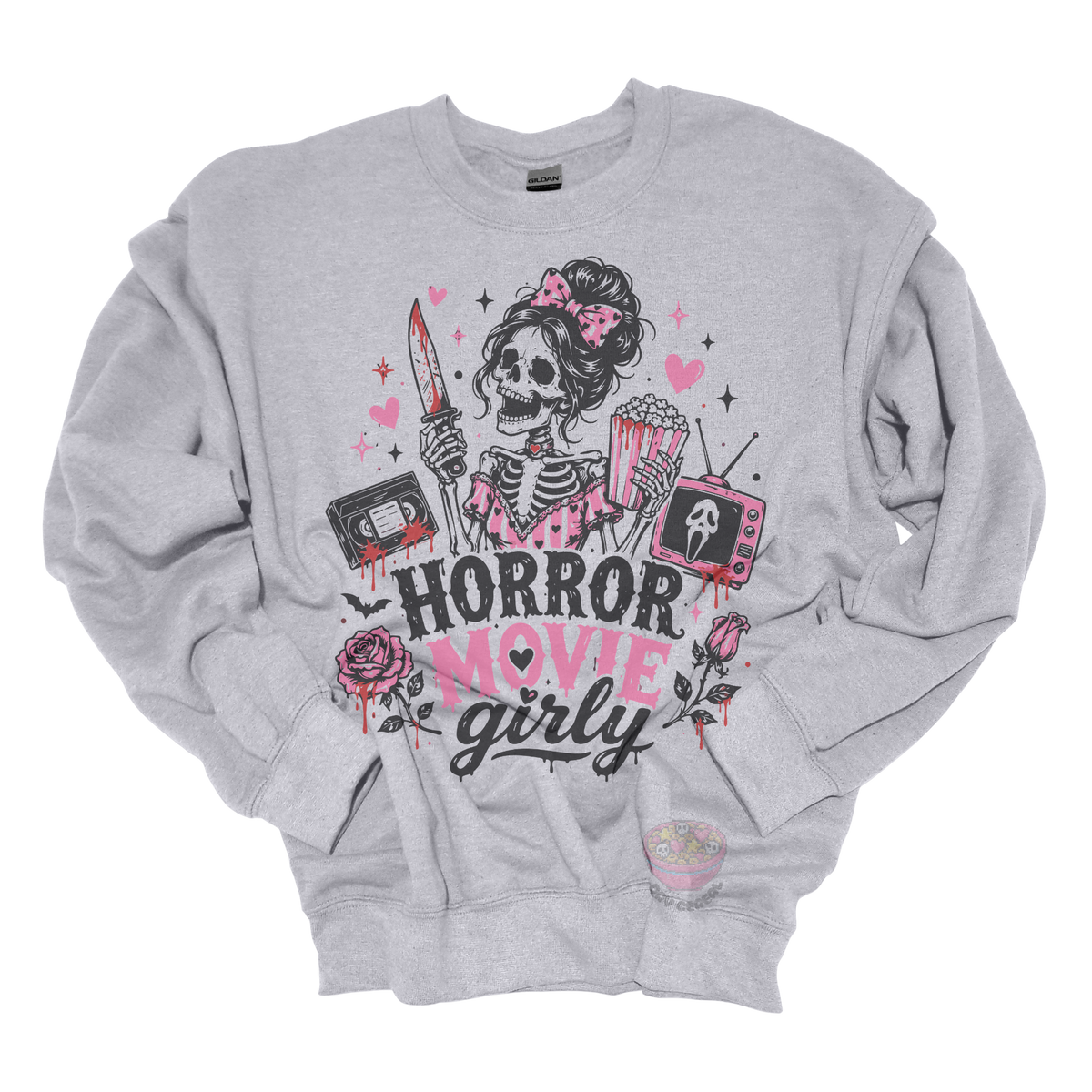 Gray crewneck sweatshirt featuring a skeleton with a pink bow holding a bloody knife and popcorn, surrounded by horror-inspired movie details, roses, hearts, a VHS tape, retro television, and the phrase "Horror Movie Girly."