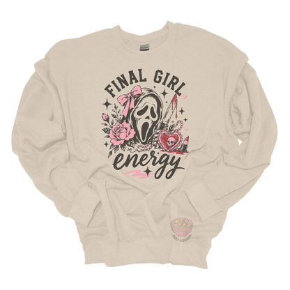 Beige crewneck sweatshirt featuring a horror-inspired ghost mask design with pink roses, a bloody knife, heart locket, lipstick, and the phrase "Final Girl Energy."