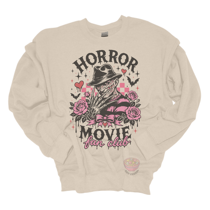 Beige crewneck sweatshirt featuring a horror-inspired burned slasher character surrounded by pink roses, bats, bows, hearts, and the phrase "Horror Movie Fan Club" in a spooky vintage design.