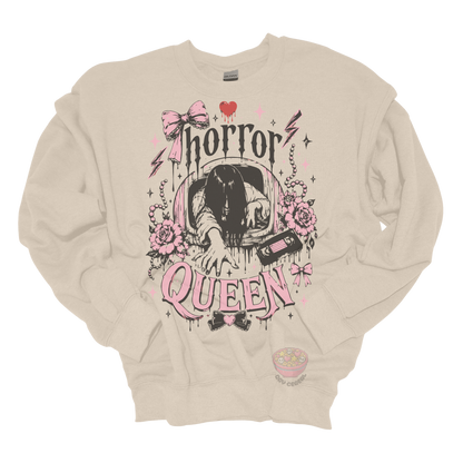 Beige crewneck sweatshirt featuring a horror-inspired long-haired ghost emerging from a television, surrounded by pink bows, roses, pearls, lightning bolts, and the phrase "Horror Queen."