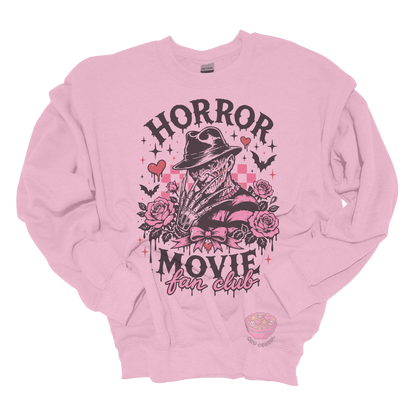Light pink crewneck sweatshirt featuring a horror-inspired burned slasher character surrounded by pink roses, bats, bows, hearts, and the phrase "Horror Movie Fan Club" in a spooky vintage design.