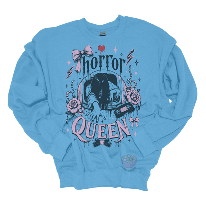 Light blue crewneck sweatshirt featuring a horror-inspired long-haired ghost emerging from a television, surrounded by pink bows, roses, pearls, lightning bolts, and the phrase "Horror Queen."