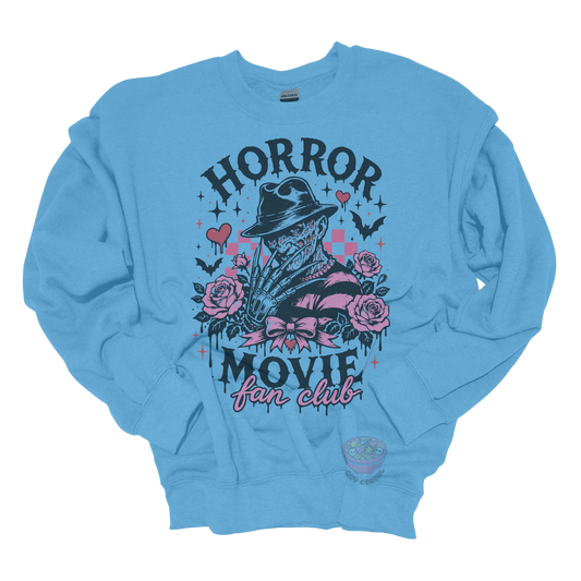 Light blue crewneck sweatshirt featuring a horror-inspired burned slasher character surrounded by pink roses, bats, bows, hearts, and the phrase "Horror Movie Fan Club" in a spooky vintage design.