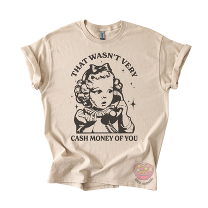 A beige graphic t-shirt featuring a black vintage-style illustration of a girl with a bow and the text 'THAT WASN'T VERY CASH MONEY OF YOU'. 