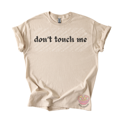 Sand unisex tee featuring the phrase "don't touch me" in bold gothic black lettering across the chest.