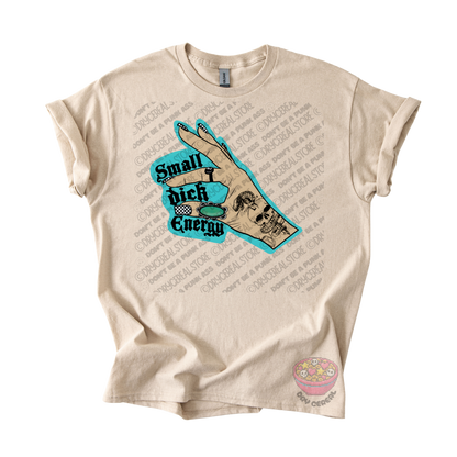 A beige graphic t-shirt featuring a hand illustration with a skull and the text 'Small dick Energy' in teal and black.