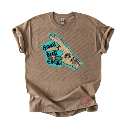 A brown graphic t-shirt featuring a hand graphic with the text 'Small dick Energy' in black with a turquoise outline, displayed on a clean white background.